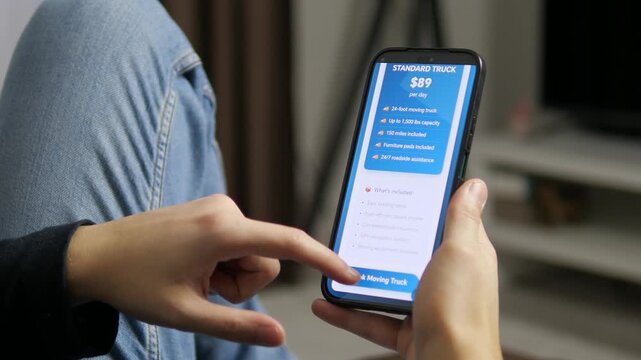 Close-up of person using mobile app to rent a professional moving truck. Features detailed UI with specifications and instant booking success alert. Ideal for transport tech and modern service promos.