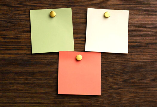 Three colorful sticky notes pinned to a dark wooden background, flat lay composition