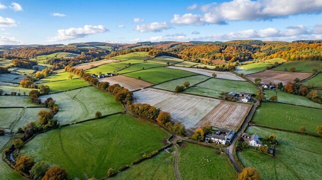 Vibrant aerial landscape photograph showcasing a patchwork of agricultural fields and rolling hills. The fields are divided into various sections, some with lush green grass and others with a light du