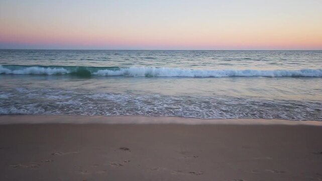 Ocean waves rolling onto a sandy beach at sunset with a curving coastline and distant headland along the Spanish coast under a clear evening sky.