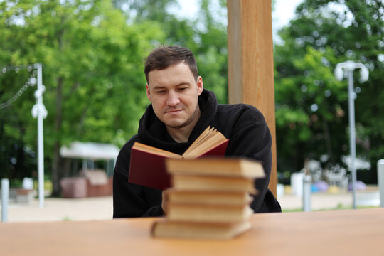 Man reading book while sitting at table. Academic student studying literature in park. Leisure activity, focus, habit of self education, hobby, knowledge acquisition and intellectual growth.