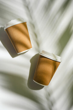 Two takeaway coffee cups with palm leaf shadows on white background, flat lay with copy space