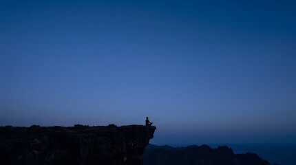 A person stands on the edge of a cliff overlooking a vast landscape at dusk. © trash