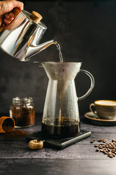 Pour hot water over coffee brewing with dripper and kettle, specialty coffee preparation, dark background, still life