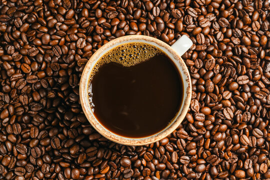 Cup of black coffee on roasted coffee beans background, top view
