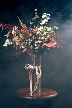 Autumn bouquet in glass vase with ribbon on stool in smoky studio