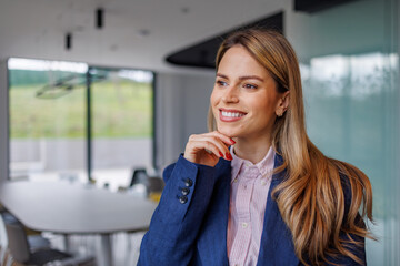 Fototapeta premium Businesswoman standing in conference room with hand on chin, smiling and contemplating future business success