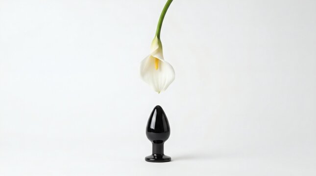 Minimalist conceptual art with a black butt plug and a white calla lily flower on a clean white background.