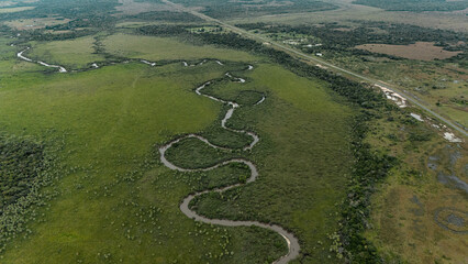 Fototapeta premium Aerial view of meandering river winding through vast green plains with highway near San Luis del Palmar, Corrientes, Argentina
