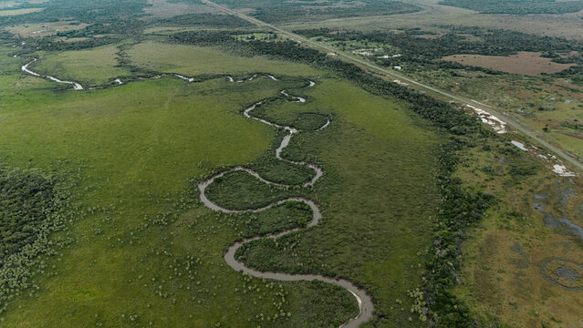 Aerial view of meandering river winding through vast green plains with highway near San Luis del Palmar, Corrientes, Argentina