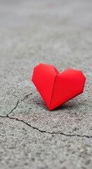 Fototapeta premium A bright red paper origami heart sits on a rough, weathered surface of cracked gray concrete, highlighting a deep symbolic contrast, heart, cracked, vulnerable