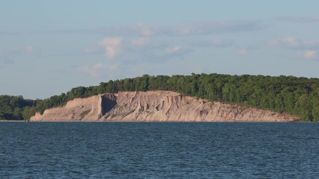 Steep sandy bluffs along the waves and lakeshore before a green forest
