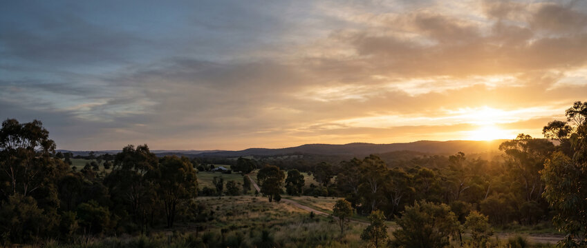 A serene sunrise over a calm Australian landscape, soft golden light breaking through, peaceful and hopeful atmosphere. Muted warm tones. The bright focal light sits on the right, with soft open sky a