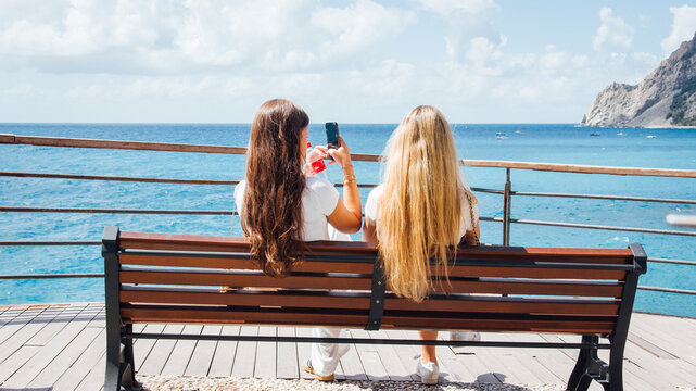 Deux jeunes femmes assises sur un banc regardant la mer m&eacute;diterran&eacute;e. Jeunes belles filles photographiant la mer.
Couple de femmes touristes en &eacute;t&eacute; sur la c&ocirc;te d'Azur.
Jeunes adultes vacances &agrave; la mer