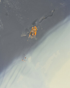 Aerial view of a rusty shipwreck stranded on the black sand beach of Solheimasandur with rippling water and dark volcanic textures in Vik, Myrdalshreppur, Iceland.