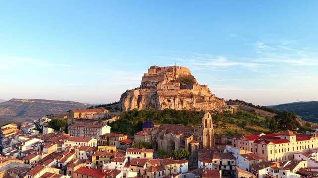 Morella castle perched on limestone rock above Gothic church of Santa Maria and medieval town rooftops at golden sunrise, Els Ports, Castellon, Valencian Community, Spain