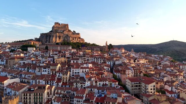 Aerial view over rooftops of medieval Morella with swifts flying, hilltop castle on rocky outcrop, Gothic church tower, Els Ports, Castellon, Valencian Community, Spain at sunrise