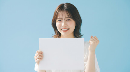 Fototapeta premium Cheerful young Japanese woman holding a blank placard and cheering on blue background