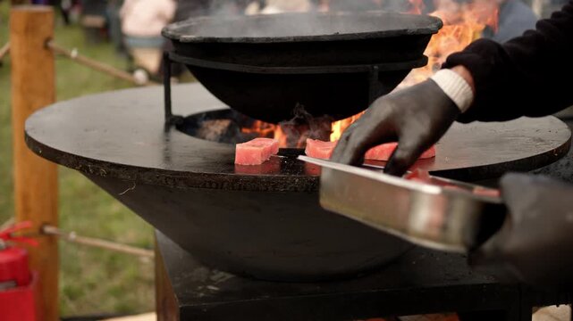 Raw fish steak cooking on a rustic metal fire pit. Salmon fillet grilling over open flames in outdoor kitchen. Culinary process of preparation fresh seafood.