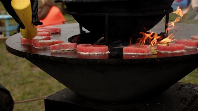 Raw fish steak cooking on a rustic metal fire pit. Salmon fillet grilling over open flames in outdoor kitchen. Culinary process of preparation fresh seafood.