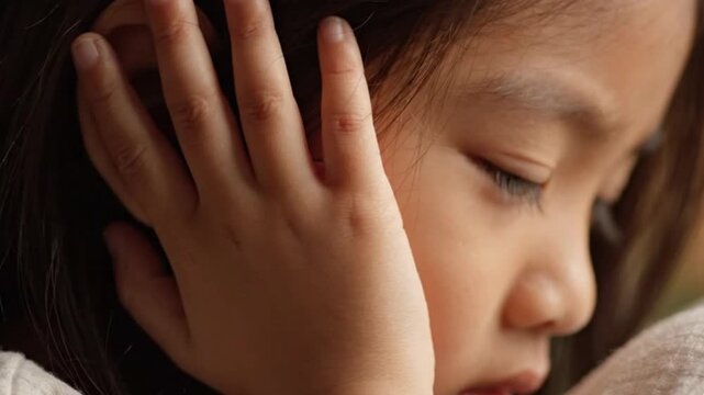 Closeup of a young girl covering her ears with her hand, expressing sensitivity to noise or distress