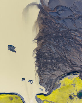 Aerial view of intricate braided patterns of glacial meltwater from Myrdalsjokull glacier flowing through dark volcanic sediment into a silty lagoon in Vik, Myrdalshreppur, Iceland.