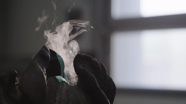 Patination process is shown on a metal surface with smoke rising in a workshop during daylight hours