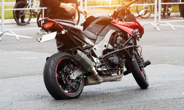 Sport motorcycle with flat rear tire on asphalt road. Person stands near damaged bike, preparing for repair or inspection of broken vehicle. Breakdown of high-performance two-wheeler.