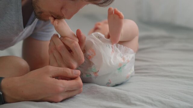 Father kissing his three month old baby son's feet. Close-up. Slow motion.