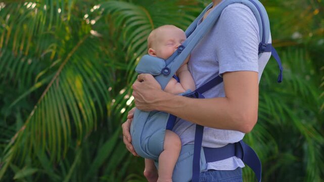 Sleeping baby son in ergonomic baby carrier during walk. Close-up. Slow motion.