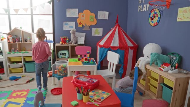 Girl holds blue foam glider and walks across a colorful playroom with blocks, toy tent, plush octopus and train set in a building; childhood joy.