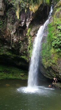 Aerial drone footage captures the impressive Cascada las Brisas waterfall cascading into a clear pool surrounded by dense green jungle foliage.