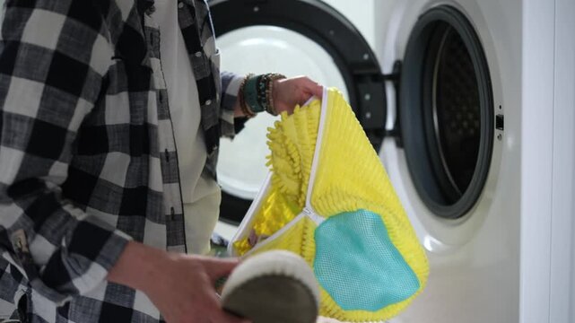 Person wearing plaid shirt places yellow microfiber mop head into front-load washing machine.
