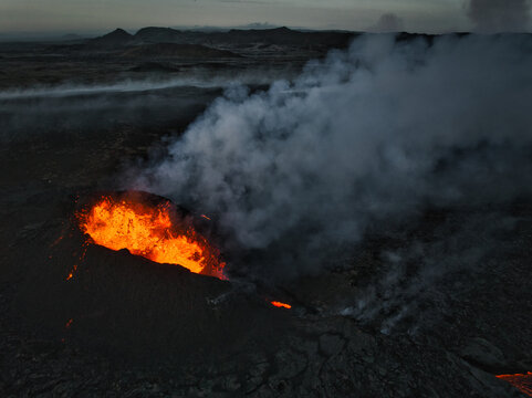 Aerial view of the Litli-Hrutur volcanic eruption with glowing orange lava and thick white smoke plumes over the dark rocky landscape in Grindavik, Grindavikurbaer, Iceland.