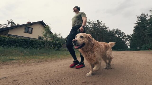 Athlete man walks with golden retriever dog on a ground path