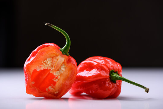 Red habanero peppers with one half cut open on dark gradient background with reflection. Fresh chili, dramatic lighting, spicy ingredient, studio shot