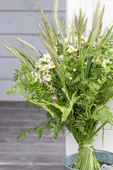 Vertical wildflower bouquet with chamomile, fern, grasses, rustic porch decor, summer solstice and Ligo mood, natural seasonal arrangement, green white yellow tones, countryside wildflower bouquet art © Olga Ionina