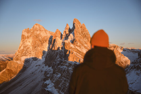 Person admiring the snow-covered peaks of Seceda at sunset in the Dolomites. Dramatic alpine landscape with rugged limestone mountains and warm evening light