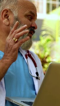 Indian doctor patient discuss case outdoors in natural greenery as senior male physician reviews medical report on laptop or looking at case file with patient during open air healthcare consultation