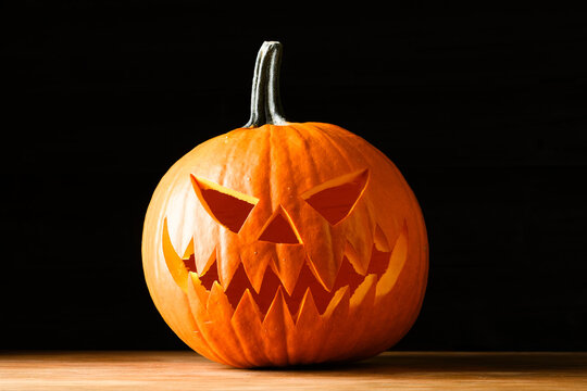 Carved Halloween jack o lantern pumpkin with spooky face standing on a wooden table against a dark background. Traditional autumn decoration with copy space for seasonal holiday designs