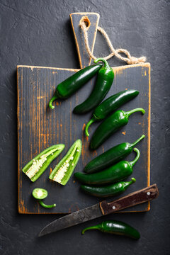 Black jalapeno with knife on rustic wooden cutting board close up. Green mexican jalapeno hot peppers