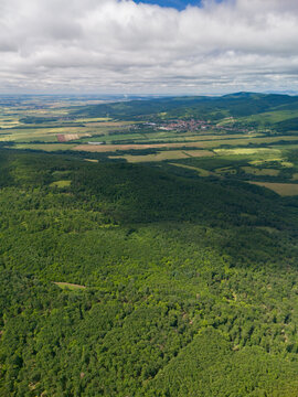 Aerial view of the lush green forests and rolling hills of Bohunicky Rohac in Stiavnicke Vrchy with a distant village and fields Bohunice, Nitra Region, Slovakia.