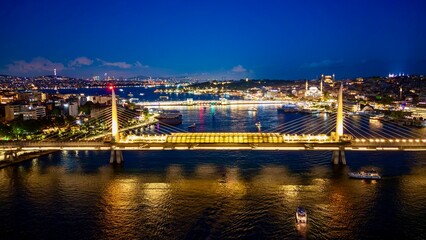 Fototapeta premium Istanbul, Turkey - June 13, 2026: Aerial drone night view of Haliç Bridge in Istanbul, Turkey, showing the bridge over the Golden Horn, city lights, waterfront districts, and reflections on the water.
