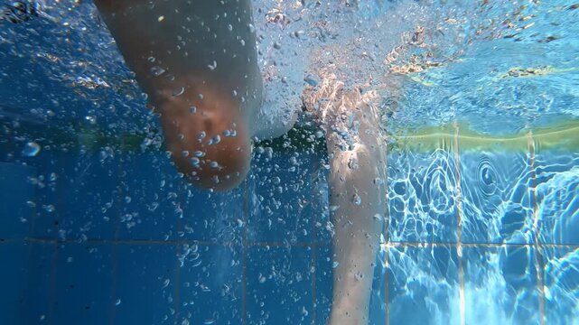 Slow motion underwater video of a girl dangles her feet in the pool water.