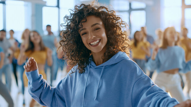 AI image Portrait of a joyful young woman with curly hair looking at camera during a modern dance class, energetic blurred group of diverse youth dancing in a bright sunny studio background