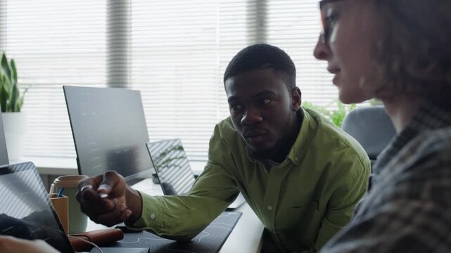 Medium shot of young adult African American man and Caucasian woman collaborating on software development in office, pointing at laptop screen. Clip for tech startup marketing or IT training videos