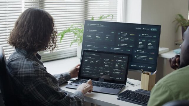 Over shoulder shot of young adult Caucasian woman pointing at laptop screen, discussing data with African American colleague. Ideal for commercial videos on software engineering and corporate teamwork