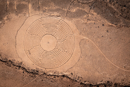 Aerial view of a large circular stone labyrinth constructed on the arid desert landscape with winding paths and textured soil El Cotillo, Canary Islands, Spain.