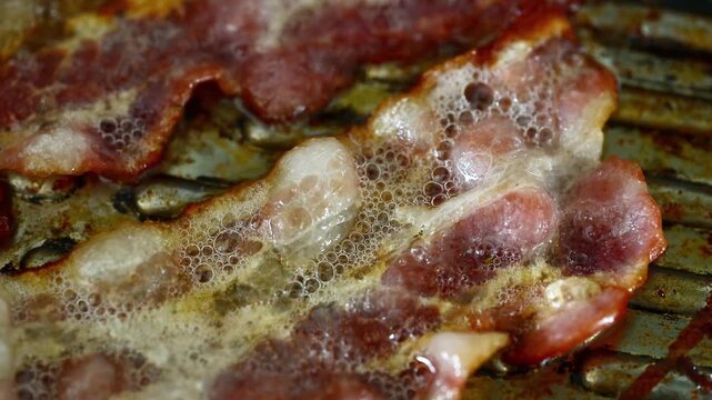 Extreme close-up of bacon frying in pan with bubbling oil, sizzling fat, unhealthy cholesterol food, crispy meat cooking, greasy breakfast, guilty pleasure, delicious but dangerous