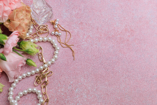 Jewelry and flowers arranged on a pink background during daytime on a table in a home setting